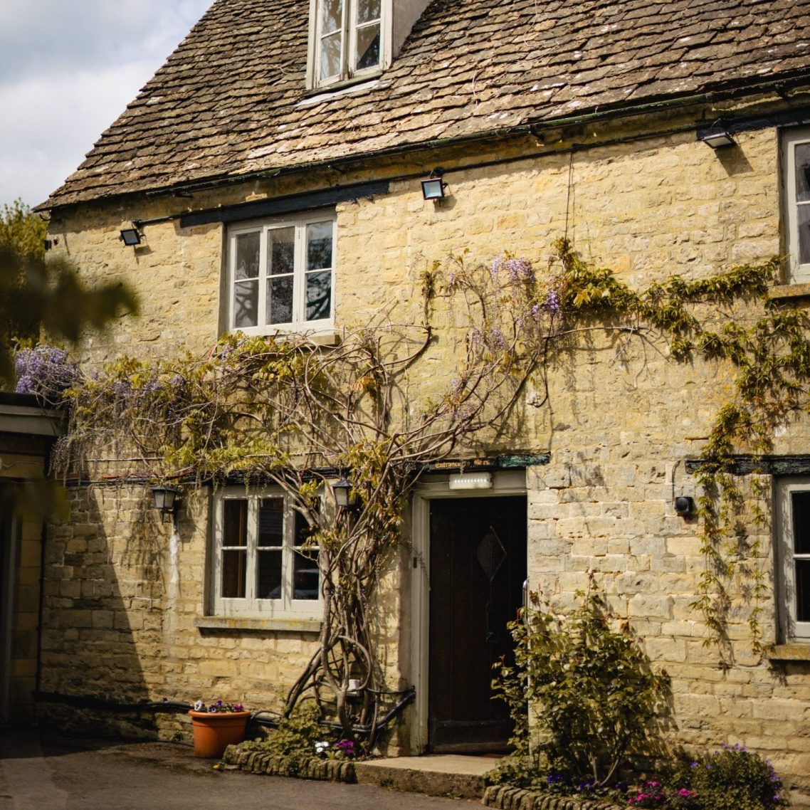 The Baker’s Arms, a historic Grade II listed stone cottage in Somerford Keynes, adorned with wisteria and a welcoming entrance.