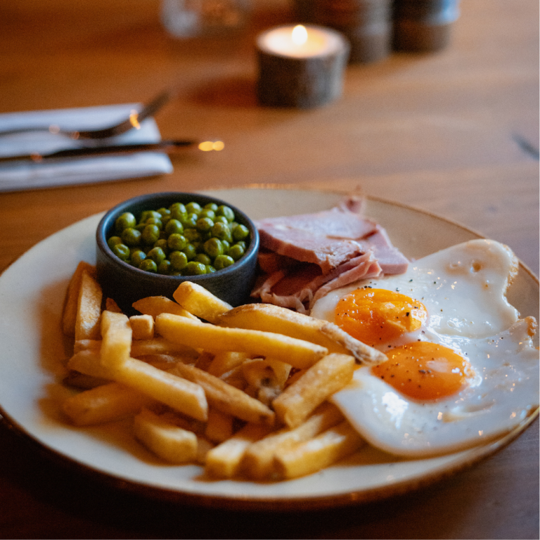 Honey and mustard glazed ham with two local free-range eggs, skin-on chips, and peas from The Baker’s Arms pub desking menu.